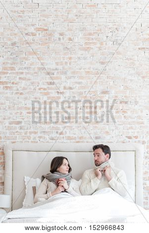 Having a bed rest. Nice cheerless young couple lying on the bed and looking at each other while having a cold
