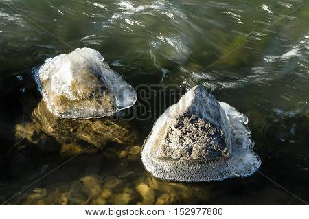 Stones covered with ice in the river. Stones in a rough stream of the river. Thaw. Thawing of ice in the river.