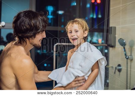 Dad Wipes His Son With A Towel After A Shower In The Evening Before Going To Sleep On The Background