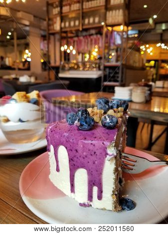 Tasty Slice Of Cake With Fresh Berries And Nuts In Cafe With Violet Glaze