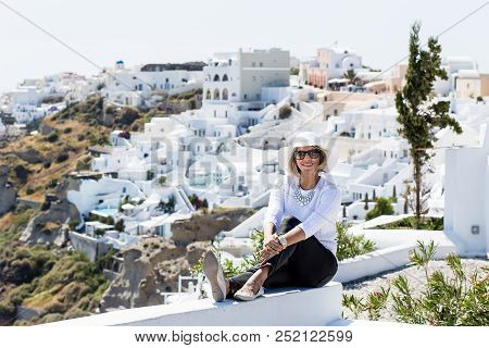 Gourgeous View Of Blond Woman In Front Of White Walled Town Of Oia In Santorini, Greece