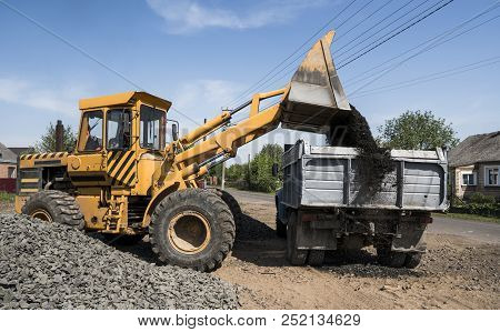 Yellow Loader Delivering Stone Gravel Into Truck During Road Construction Works. The Stones For The 