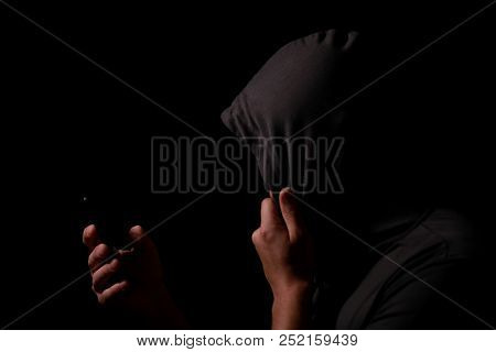 Silhouette Of The Unknown Person In A Hood With The Mobile Phone In A Hand In The Dark. Cyber Crimin