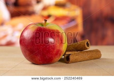 One Whole Fresh Red Apple James Grieve Variety With Cinnamon Sticks With Rustic Wood Kitchen In Back