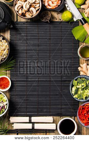 Asian Cuisine Ingredients On Bamboo Mat Over Old Wooden Background, Top View. Vegetables, Spices, Sh