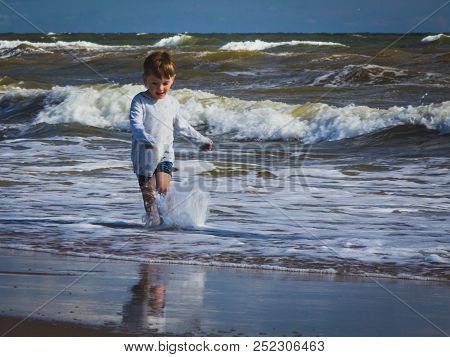 Wholesome Kid With Wet Clothes Runs On The Beach In Seawater.