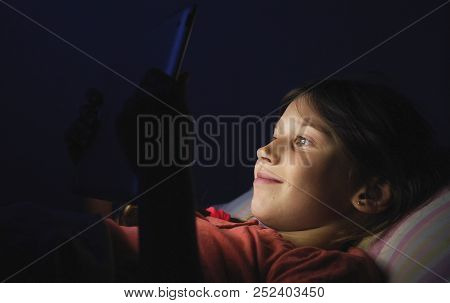 Caucasian Girl Lying In Bed Playing Tablet In Social Internet In Dark Blue Light Under Blacket. Chil