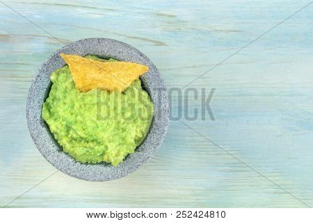 An Overhead Photo Of Guacamole Sauce In A Molcajete, Traditional Mexican Mortar, On A Teal Blue Back