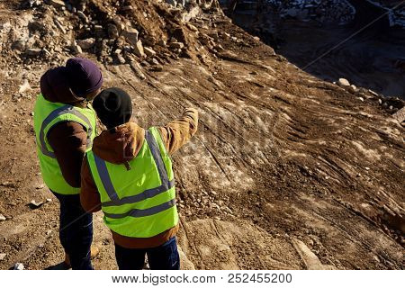 Back View Portrait Of Two Industrial Workers Wearing Reflective Jackets, One Of Them African, Standi