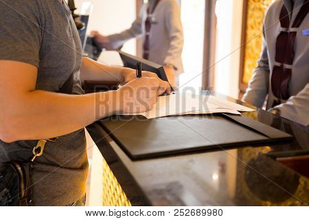 Male Guest Check In At Hotle Signing A Form At Reception Counter.