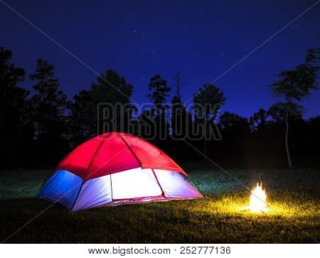 Stars Shining Above A Small Lighted Tent And Campfire