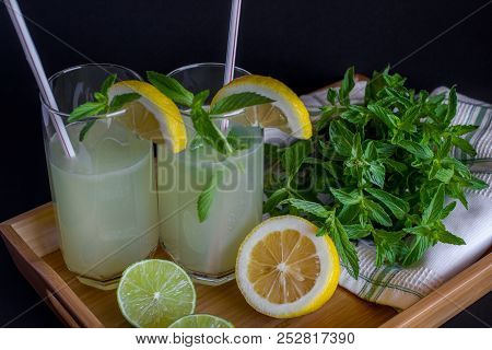 Homemade Citrus Lemonade In Glasses With Straws With Mint Leaves And A Bunch Of Mint, Lemons, Limes 