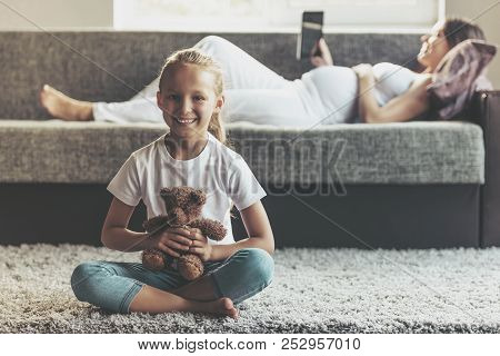 Little Smiling Girl Holding Teddy Bear. Looking At Camera And Smiling. On Background Pretty Pregnant