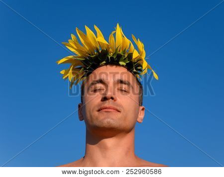 A Man With A Naked Torso In A Field Of Sunflowers. Flower Of A Sunflower On The Head. The Sunflower 
