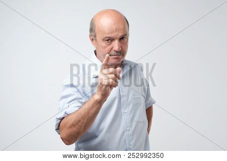 Portrait Of Serious Senior Man With Warning Finger And Blue Shirt Shirt Against Light Gray Backgroun