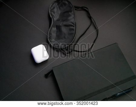 Flat Lay Of Black Notebook, Black Mask For Sleep And Wireless Headphones On Black Background