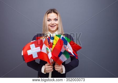 Cheerful Young Woman With A Large Set Of Flags Of Different Countries Of The World. Polyglot, And Le