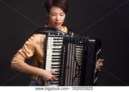 A Brunette In A Gold Shirt, With Short Haircut, On A Dark Kground Of The Studio. Play The Accordion