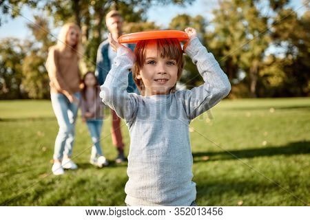 Portrait Of Happy Family Of Four Going To Play With Disc On A Green Meadow With Grass. Focus On Cute