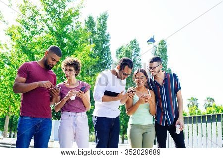 Happy People In Casual Using Smartphones Outside. Men And Women Standing Together And Showing Phone 