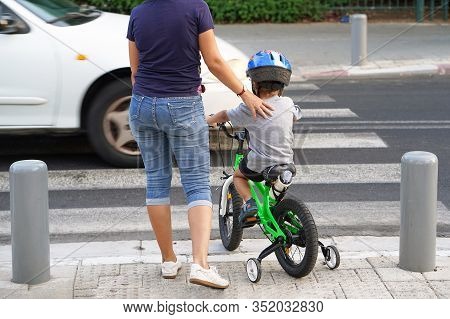 Mother Goes Pedestrian Crossing With Childr On Bicycle. A Woman With Son Crossing The Road In The Ci