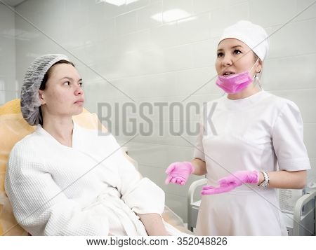 Woman Wearing Disposable Medical Bathrobe Being At Consultation In Cosmetology Clinic. Attractive Fe