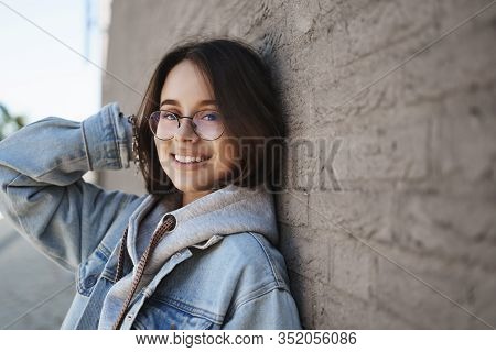 Close-up Side Portrait Of Adorable Young Queer Woman In Glasses, Lean Brick Wall Outdoors On Street,