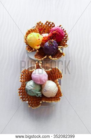 Two Huge Waffle Bowls With Ice Cream Balls In Pink, White And Green Colors And Fruit Sorbet In Yello