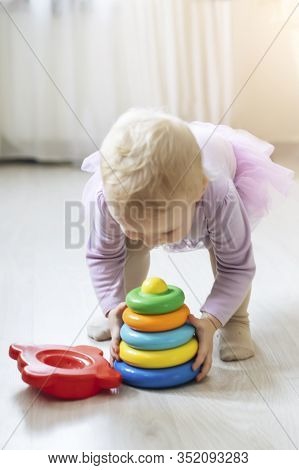 Girl Carries Toy Pyramid. Child In Living Room Sun-drenched. Educational Toys For Children Under 2 Y