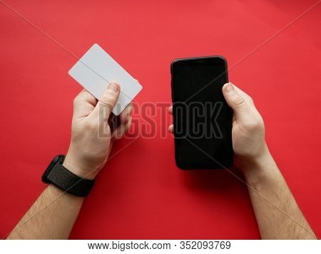 Hand With Smart Watch Holding White Card And Smartphone On Red Background. Cashless Payment, Online 
