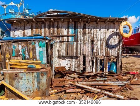 Shabby Small Building Among Lot Of Board With Old Orange Life Saver On Edge Of Roof And Clear Blue S