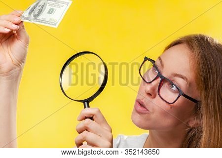 The Concept Of Checking Counterfeit Money. A Blond Woman With Interest In Looking At A Dollar Bill T
