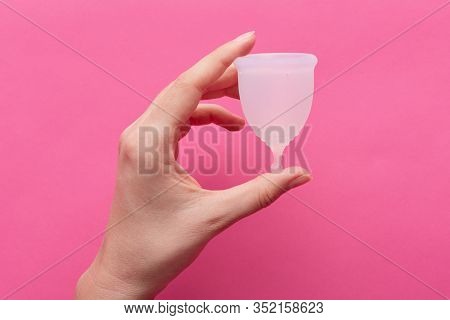 Faceless Portrait Of Young Woman's Hand Holding Menstrual Cup Isolated Over Pink Background. Menstru