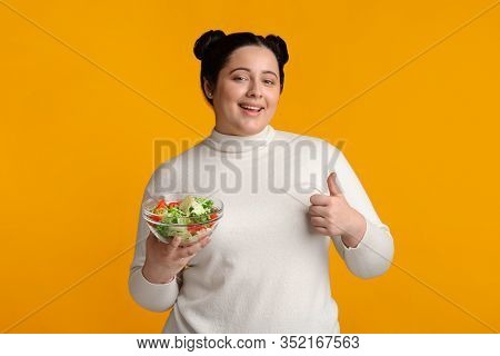 Healthy Nutrution Concept. Positive Oversized Woman Holding Bowl With Fresh Vegetable Salad And Show