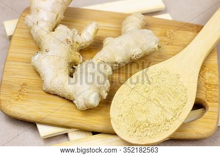 Fresh Raw Yellow Ginger Root With Ground Dry Powder In Wooden Spoon And On Wood Background.