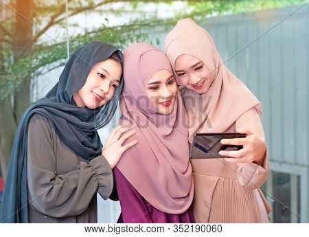 Three beautiful muslim womae wearing hajab,using mobile phone for taking photo together,model posing