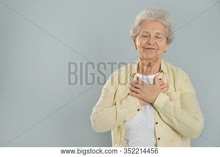 Grateful Senior Woman With Hands On Chest Against Grey Background. Space For Text