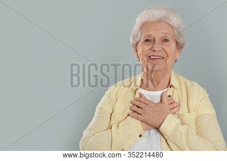 Grateful Senior Woman With Hands On Chest Against Grey Background. Space For Text