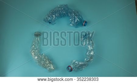 Three Crashed Plastic Bottles On Blue Background Form Resycling Sign. Plastic Utilisation Concept. A