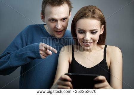 Man With The Girl Excitedly Looking At The Smartphone. Are In An Agitated State. Emotions Of Experie