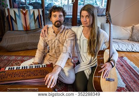 Young Shamanic Woman With Hand On Male Shoulder Sitting With Musical Instruments Like Classical Guit