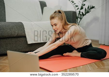 Cheerful Caucasian Girl Making Yoga On The Floor While Looking At Computer For Some Exercises