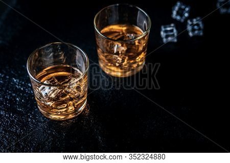 Whisky, Whiskey, Bourbon Or Cognac With Ice Cudes On Black Stone Table