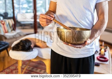 Massage Therapist Standing With A Singing Bowl In Hands And Giving A Sound Massage, To His Client Ly