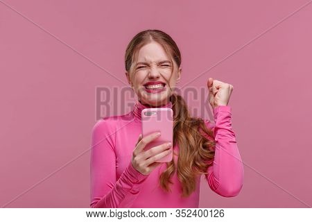 The Best Day Ever. Surpised Young Redhead Woman Holding Pink Smartphone, Smiling And Expressing Posi