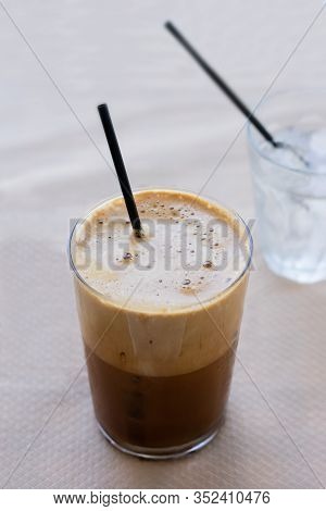 Cold Frappe Coffee With Ice Cubes On Glass With Black Straw Served On The Table In Caffeteria. Ice C