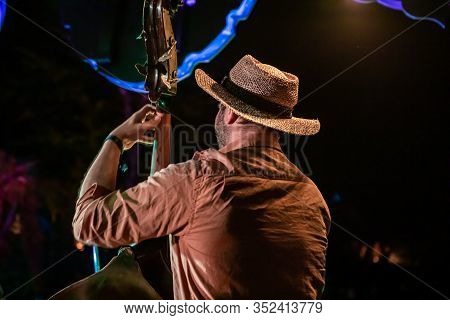 A Middle Aged Man Wearing A Straw Hat Is Seen From Behind In Selective Focus, Playing Double Bass Gu