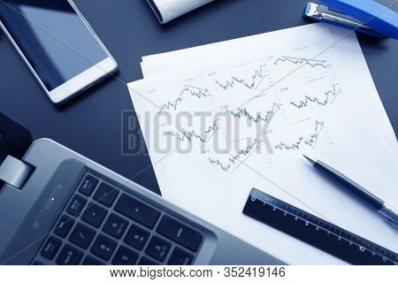 Top View Of Business Chart On Black Table With With Laptop, Phone, Pen, Ruler And Stapler