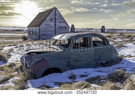 Neidpath, Sk, Canada- Feb. 20, 2020: Abandoned Austin A40 Somerset Car And Church On A Snowy Hillsid