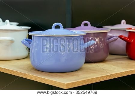 Many Enameled Steel Metal Multicolored New Modern Cooking Pots Stand On A Shelf In The Kitchen. Hous